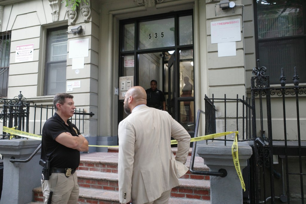 Crime scene tape draped over the railings of a building where a 27-year-old woman was found dead, with two men standing outside.