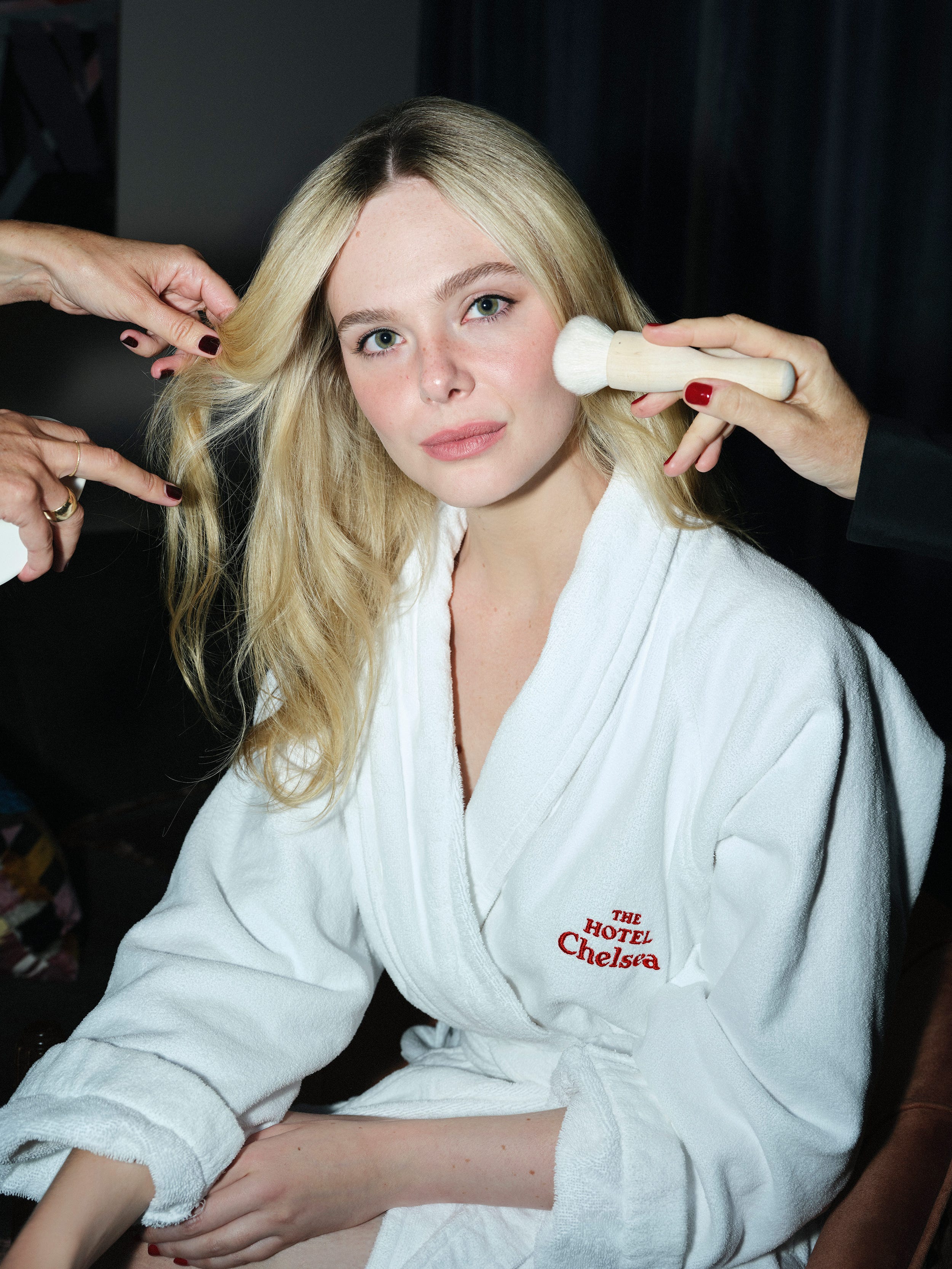 Young woman in a white bathrobe having her makeup applied while her hair is styled.