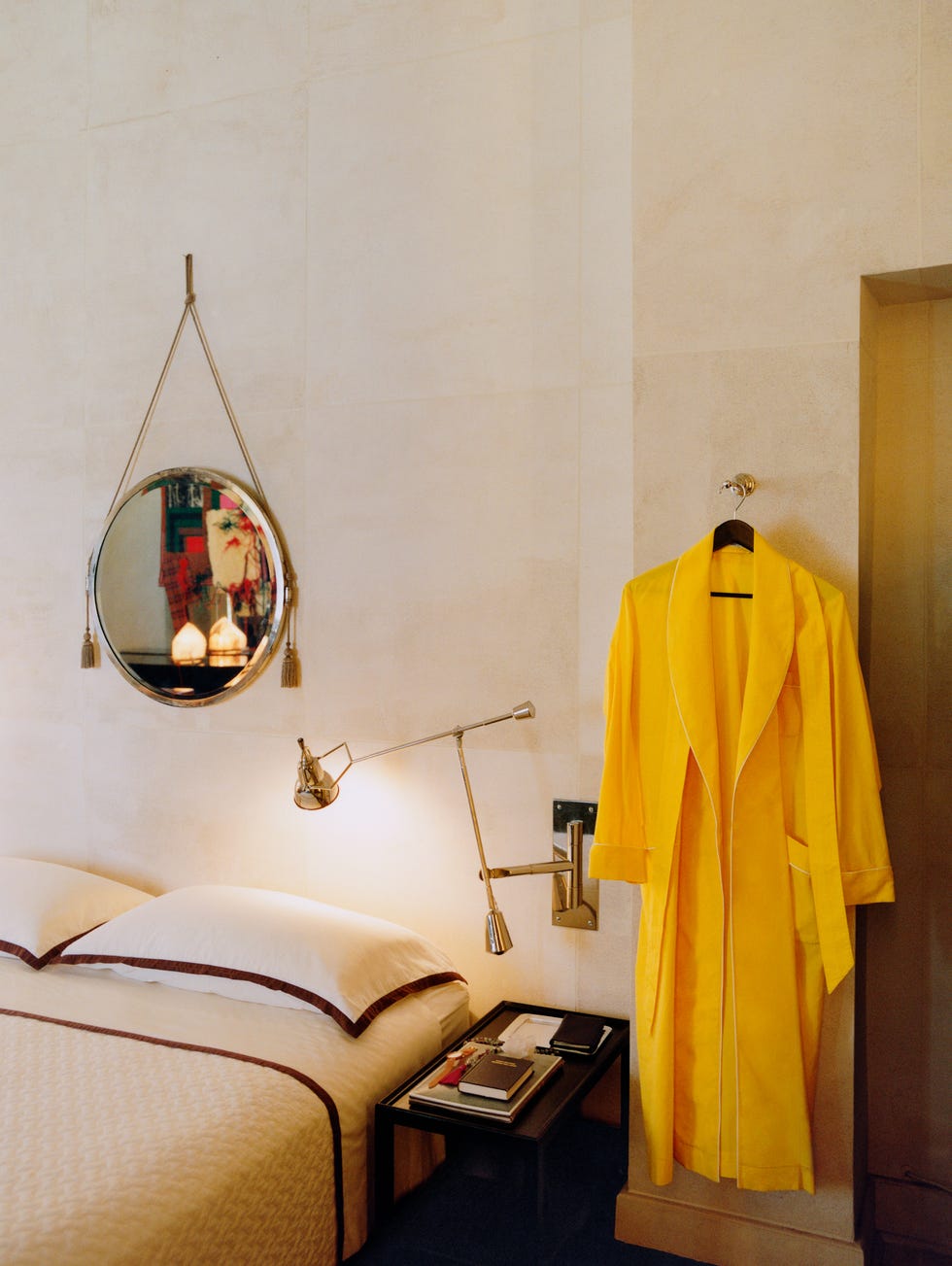 A cozy bedroom featuring a yellow bathrobe, a bedside lamp, and a round mirror on the wall.