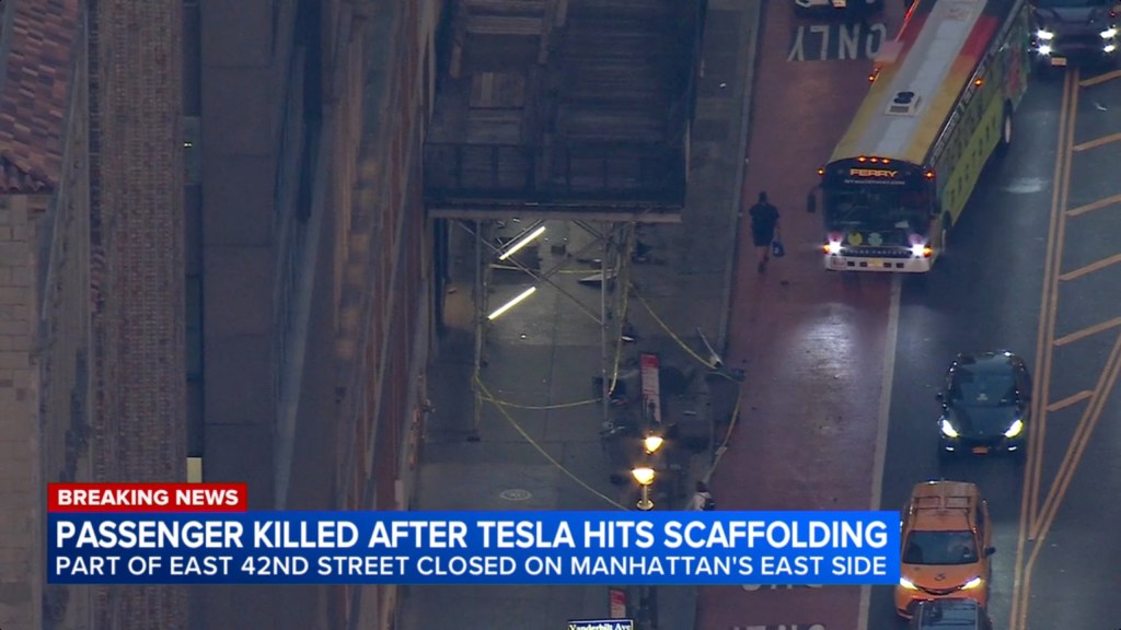 Overhead view of a street at night, with scaffolding on the left and a bus and cars on the right.