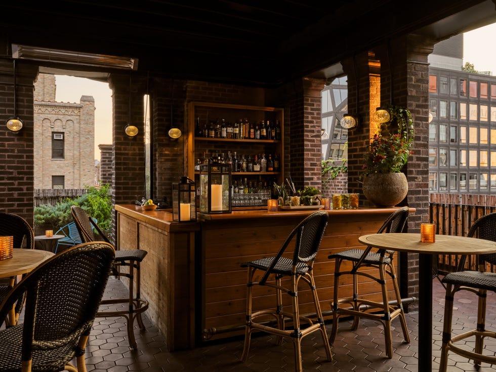 Stylish bar area with wooden counter, bar stools, and a view of a city building through open windows.
