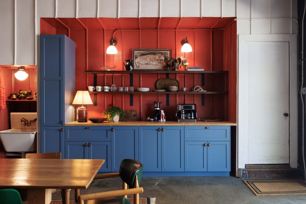 Modern kitchen with blue cabinetry, wooden countertops, red wall accents, and a dining area.