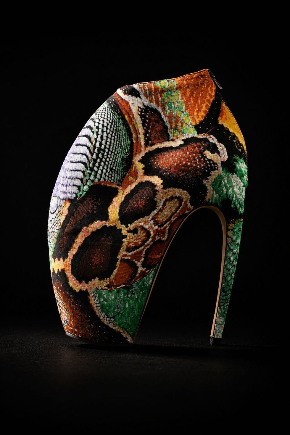 High-heeled shoe with a colorful, textured pattern resembling animal skin, set against a dark background.