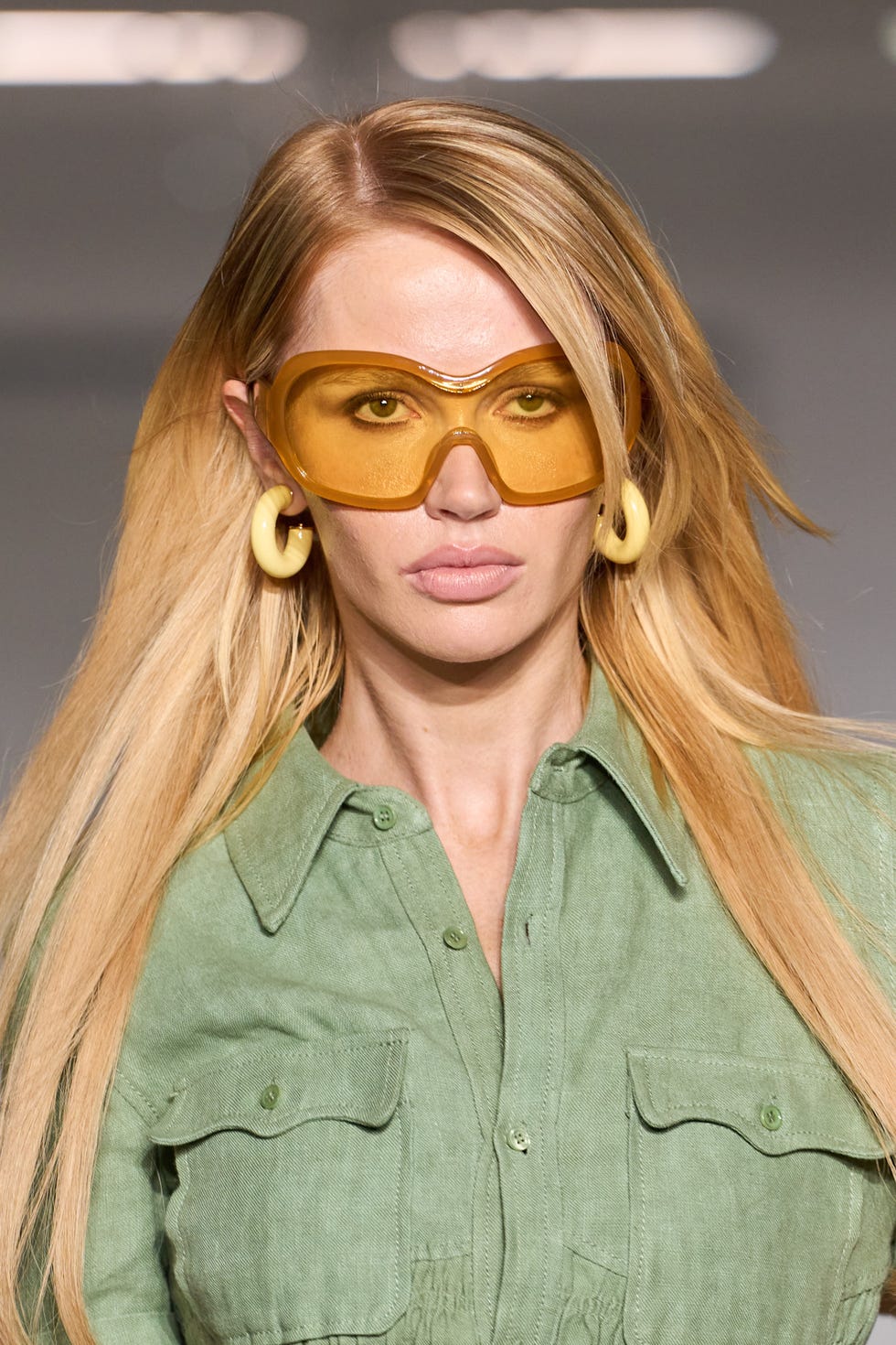Model wearing oversized yellow sunglasses and a green button-up shirt, showcasing a fashion look. Model wearing oversized yellow sunglasses and a green button-up shirt, showcasing a fashion look.
