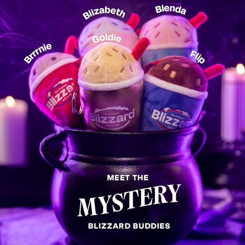Five plush dessert characters labeled with names, arranged in a black cauldron with candles in a purple setting. Five plush dessert characters labeled with names, arranged in a black cauldron with candles in a purple setting.