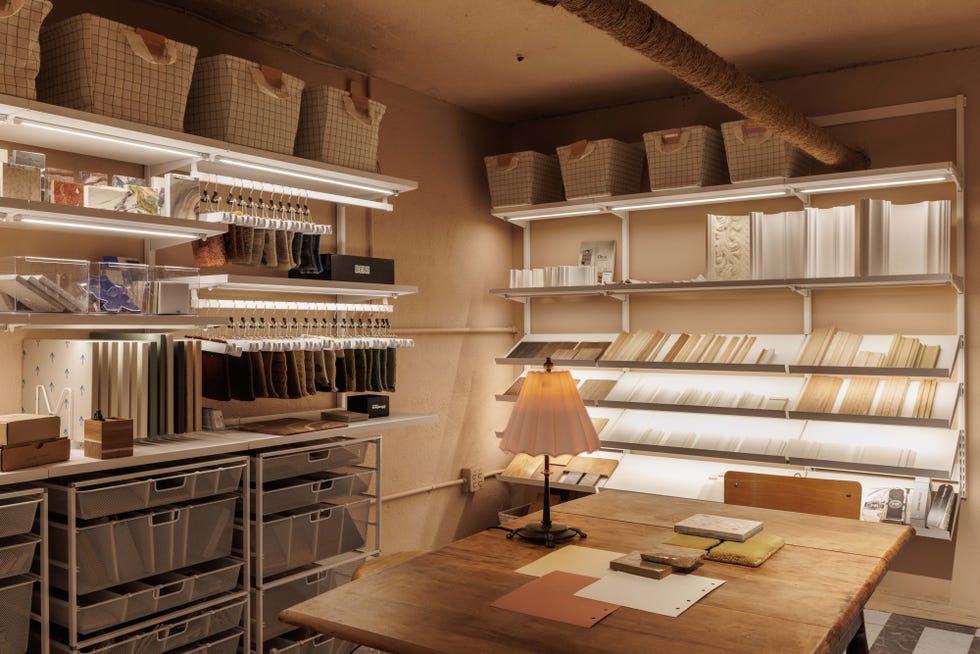 Interior design studio featuring organized shelves with materials, fabric samples, and a lamp over a wooden table.