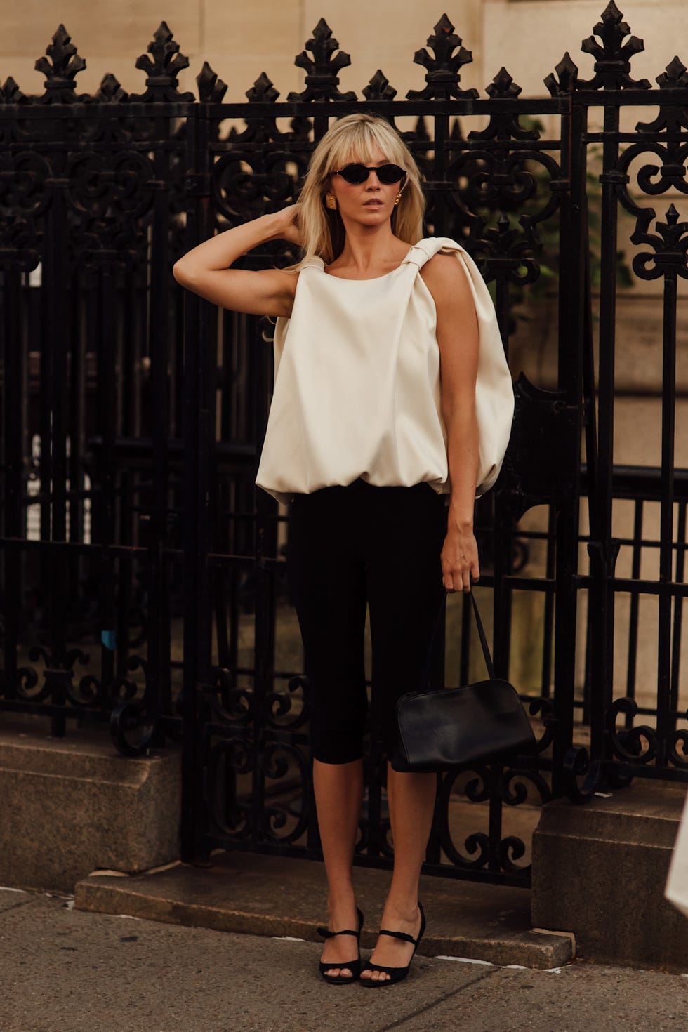 Woman in stylish clothing with a white top and black pants, standing by an ornate black gate. Woman in stylish clothing with a white top and black pants, standing by an ornate black gate.