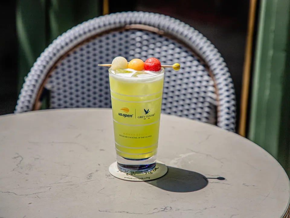 Colorful cocktail with fruits served in a glass on a table, with a patterned chair in the background.
