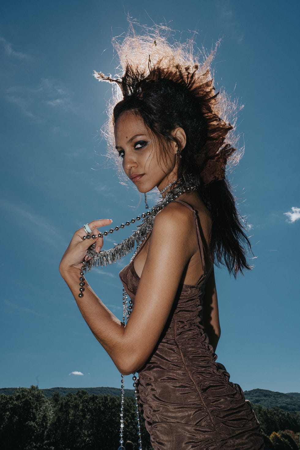 Model posing dramatically outdoors with unique hairstyle and jewelry against a bright blue sky. Model posing dramatically outdoors with unique hairstyle and jewelry against a bright blue sky.