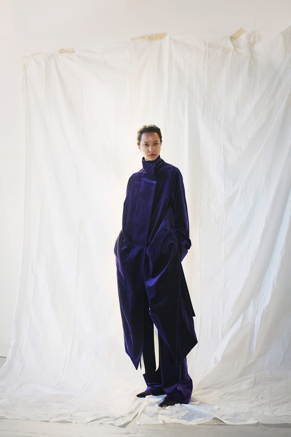Model wearing an oversized purple velvet outfit against a white backdrop.