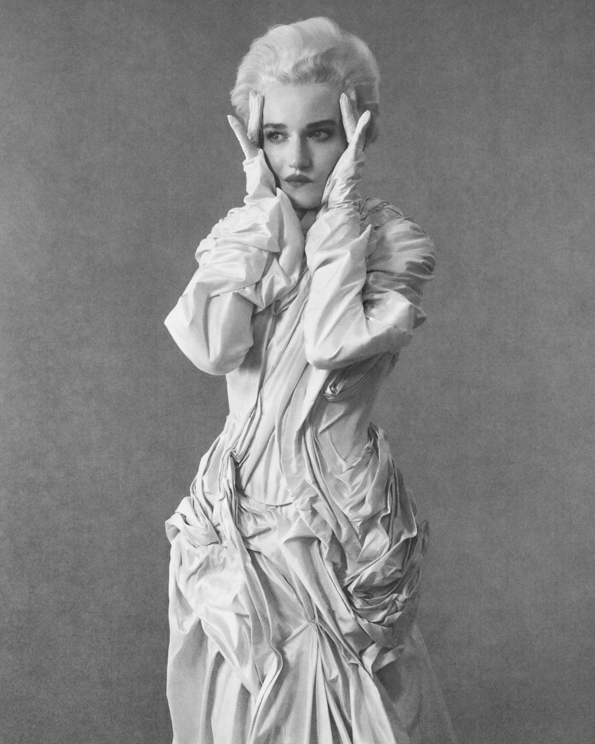Julia Garner posing dramatically in a textured white gown against a grey background, emphasizing fashion and artistry. Julia Garner posing dramatically in a textured white gown against a grey background, emphasizing fashion and artistry.