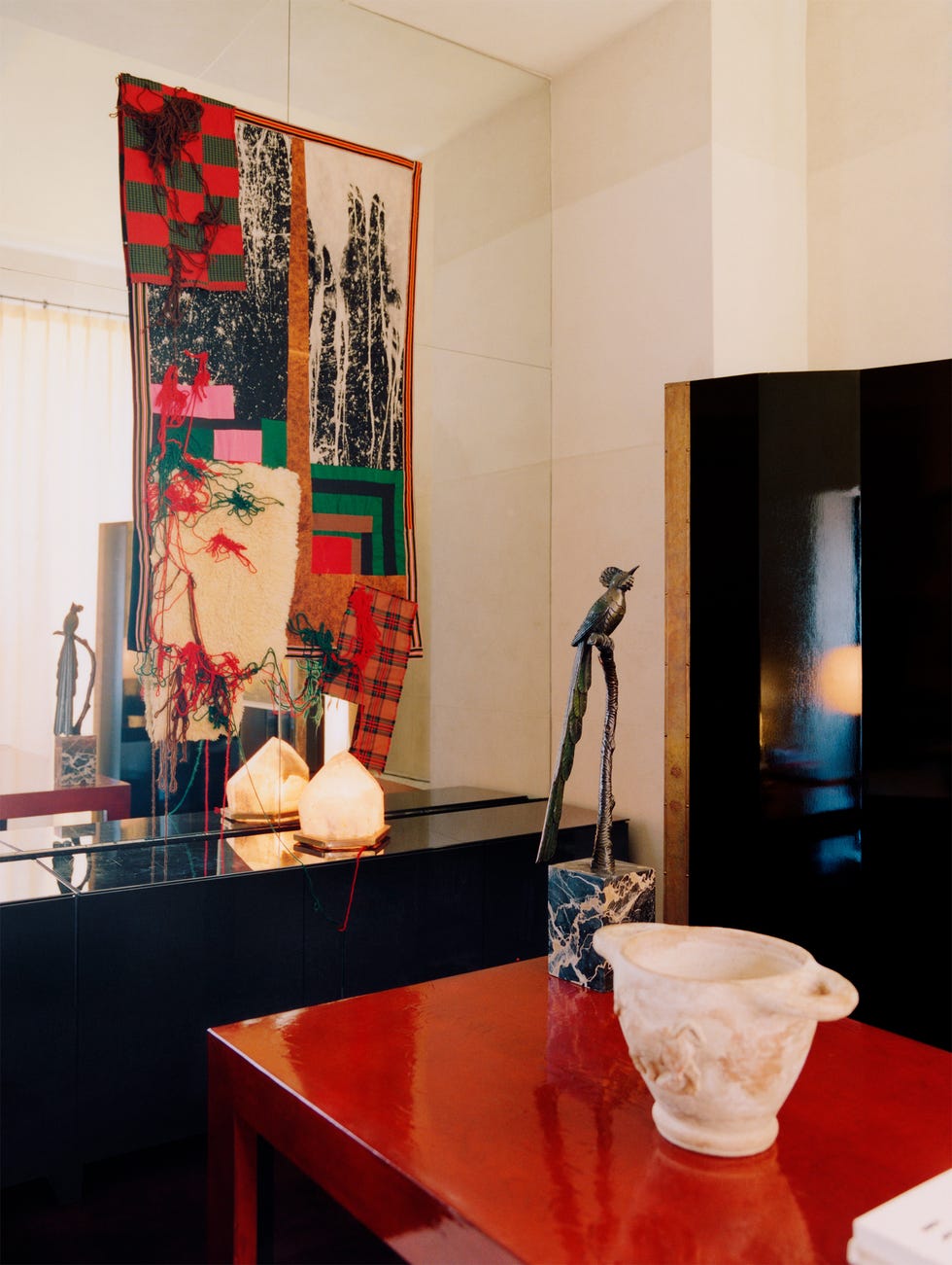 Colorful artwork hangs on the wall above a table with a marble sculpture and a decorative bowl in a modern interior setting.