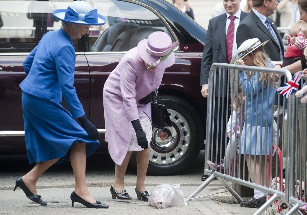 Queen Elizabeth II bending down to retrieve a bouquet of flowers she dropped during a visit to Eton College