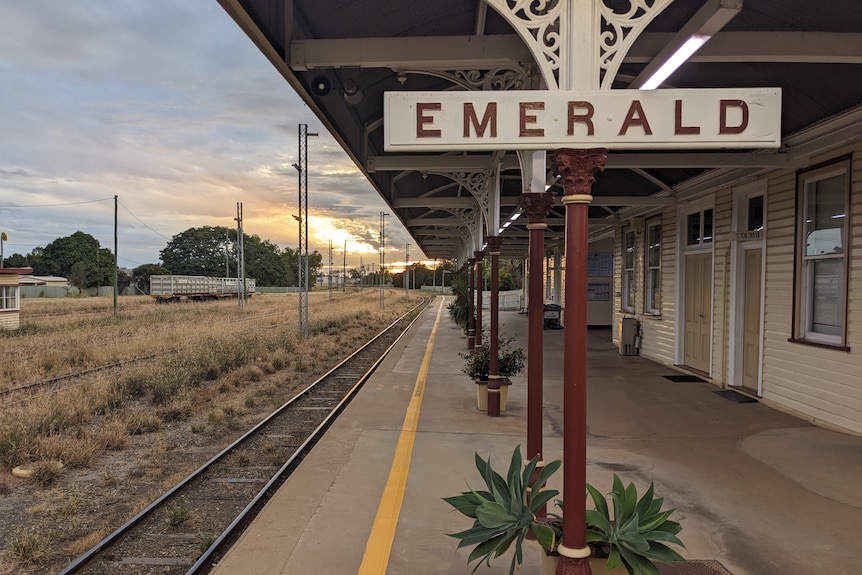 Emerald Train Station platform with "Emerald" sign and sunset in background.