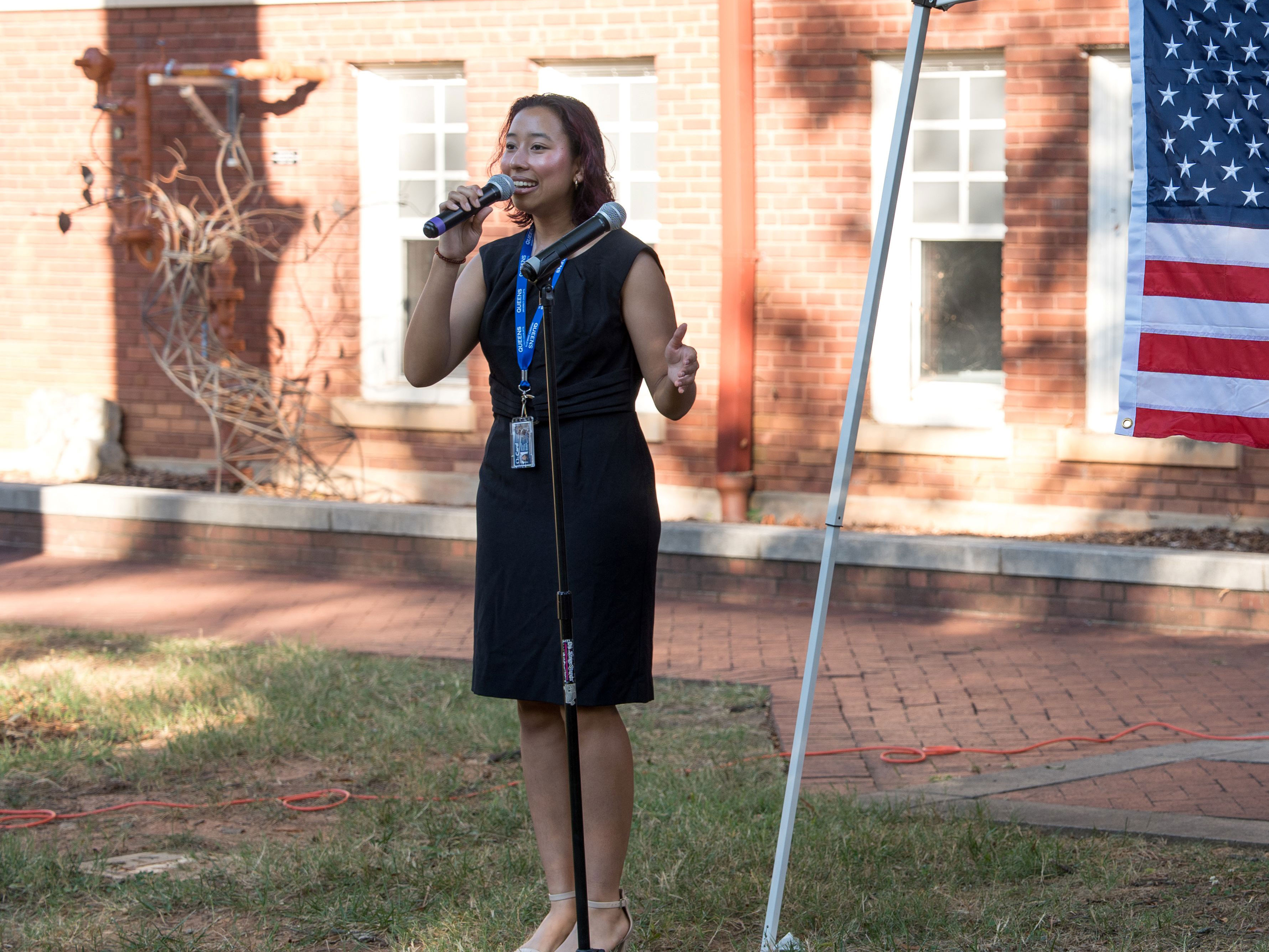 A girl in a black dress holds a microphone and sings. 