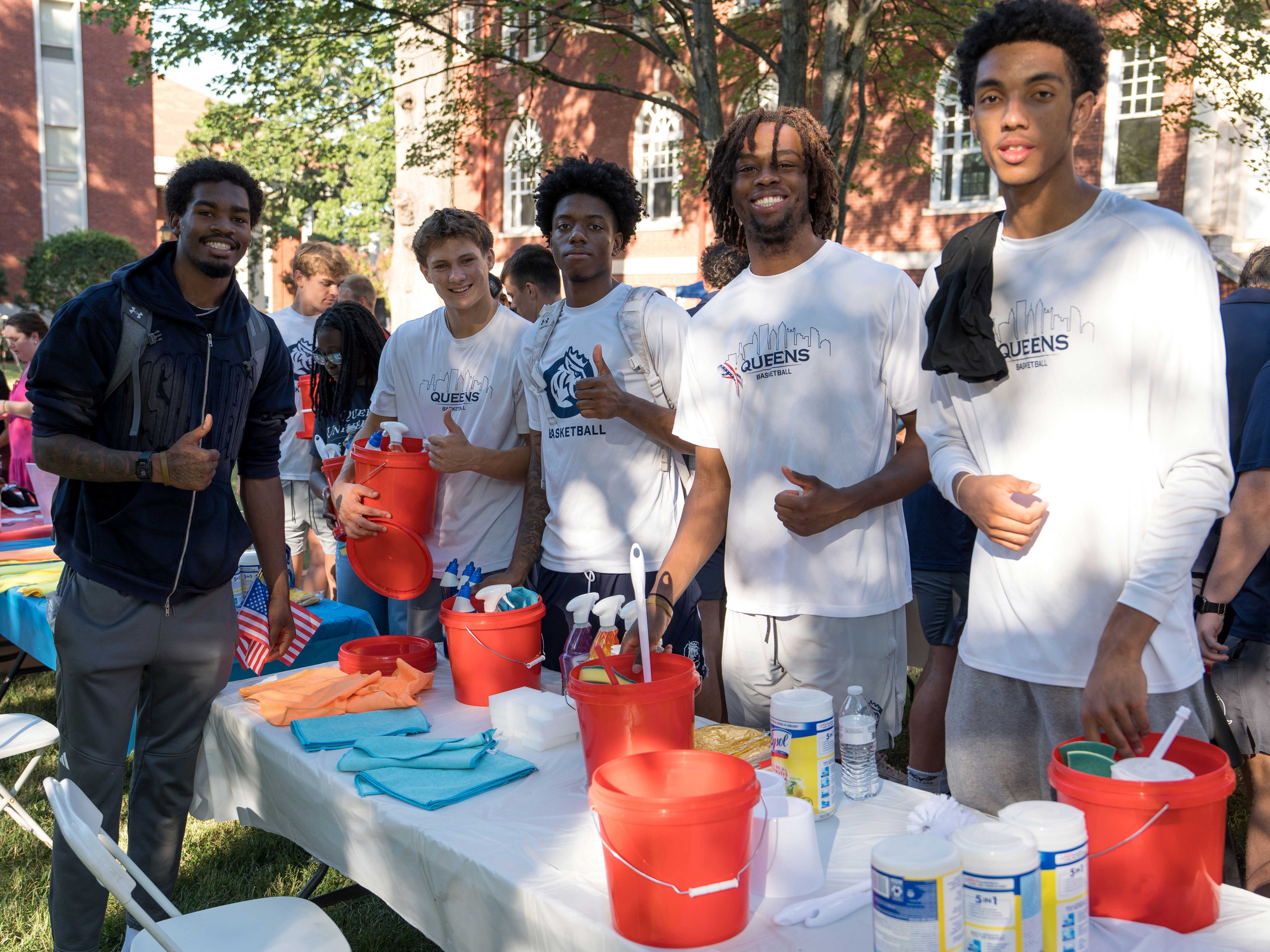 Five students stand aroudn a table assemble small red bucks of cleaning supplies. 