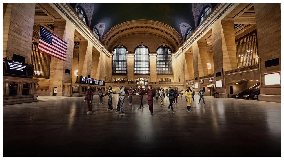A bustling Grand Central Terminal with diverse individuals in colorful attire and an American flag prominently displayed.