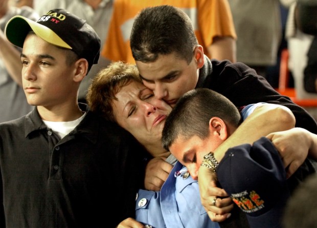 In this Friday, Sept. 21, 2001 file photo, Carol Gies, center, a wife of a missing firefighter, leans on son Ronnie as she is consoled by sons Bobbie, right, and Tommy, behind, during the ceremonies for the victims of the World Trade Center prior to the New York Mets game against the Atlanta Braves at Shea Stadium in New York. (AP Photo/Bill Kostroun, File)