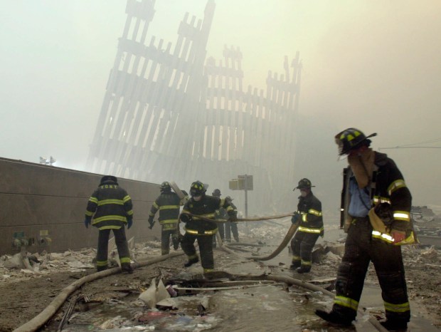 In this Sept. 11, 2001 file photo, with the skeleton of the World Trade Center twin towers in the background, New York City firefighters work amid debris on Cortlandt St. after the terrorist attacks. (AP Photo/Mark Lennihan, File)