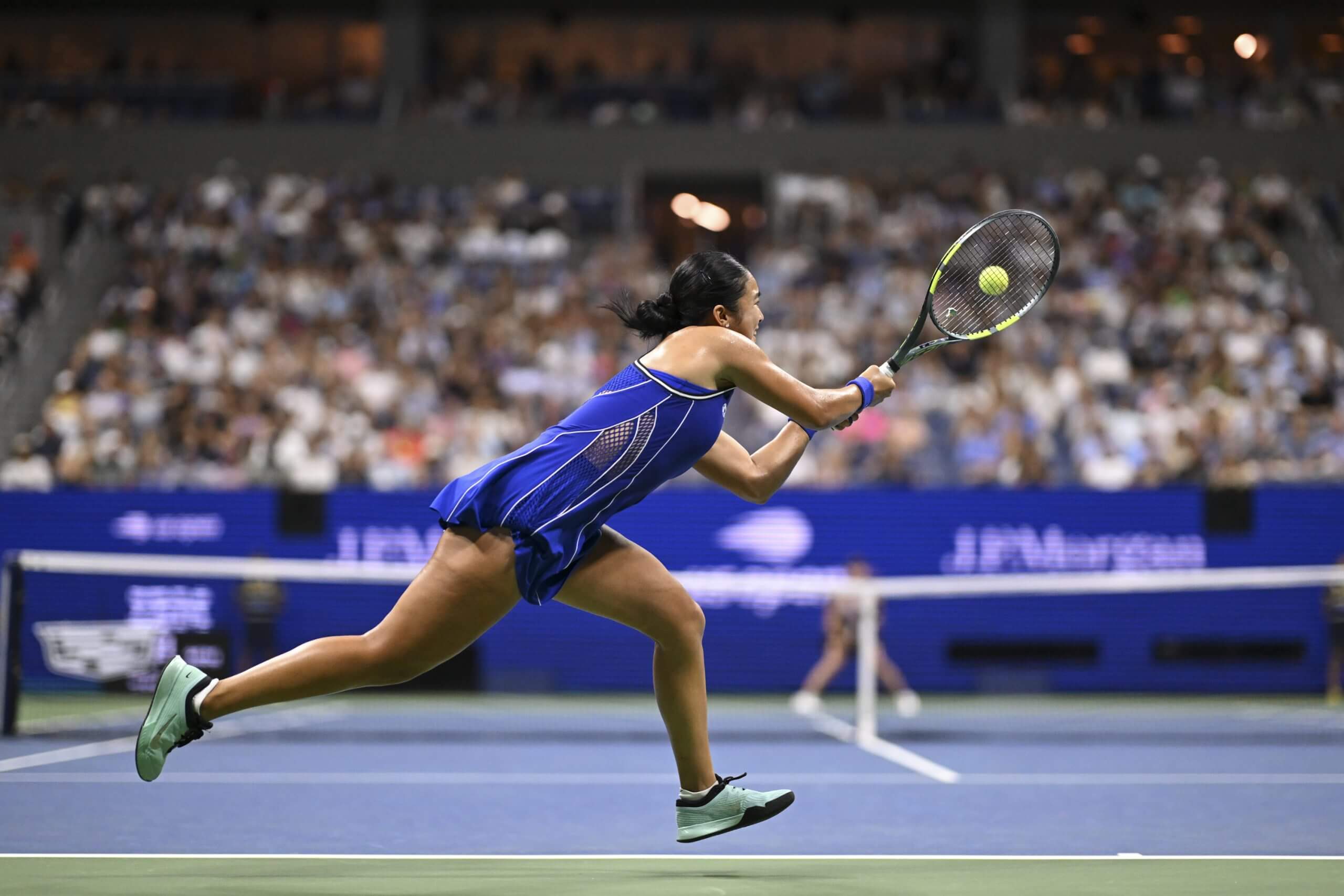 Alex Eala hits a two-handed backhand on a blue-and-green tennis court.