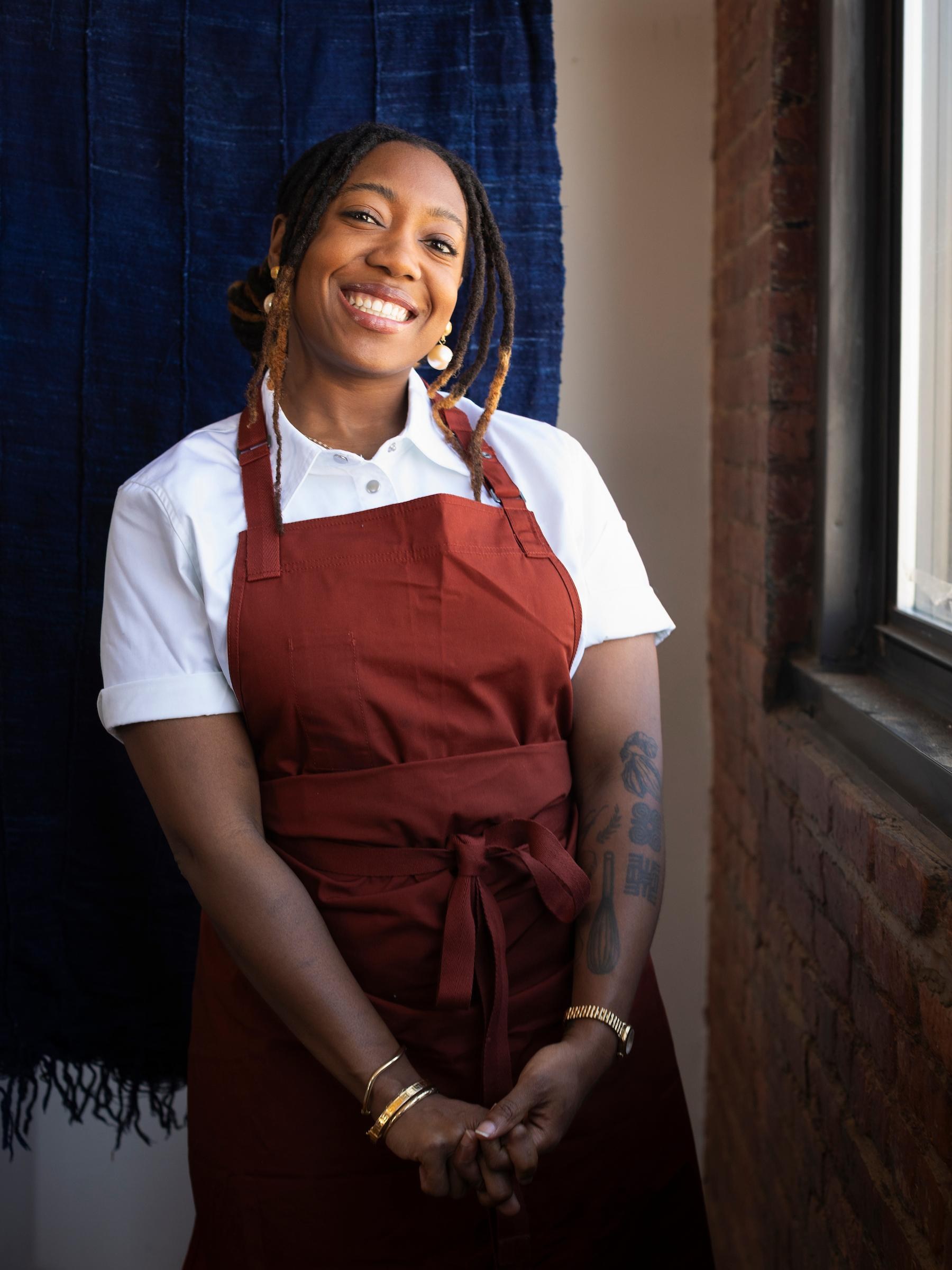 A person standing in a maroon apron and white shirt smiling.