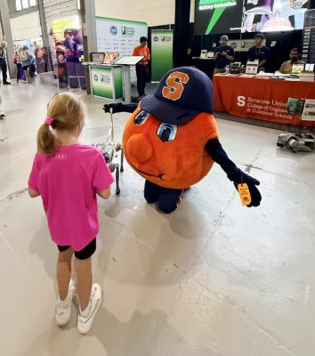 Otto the Orange plays with a small robot beside a young child at an "Energy Storage Engine" event booth.