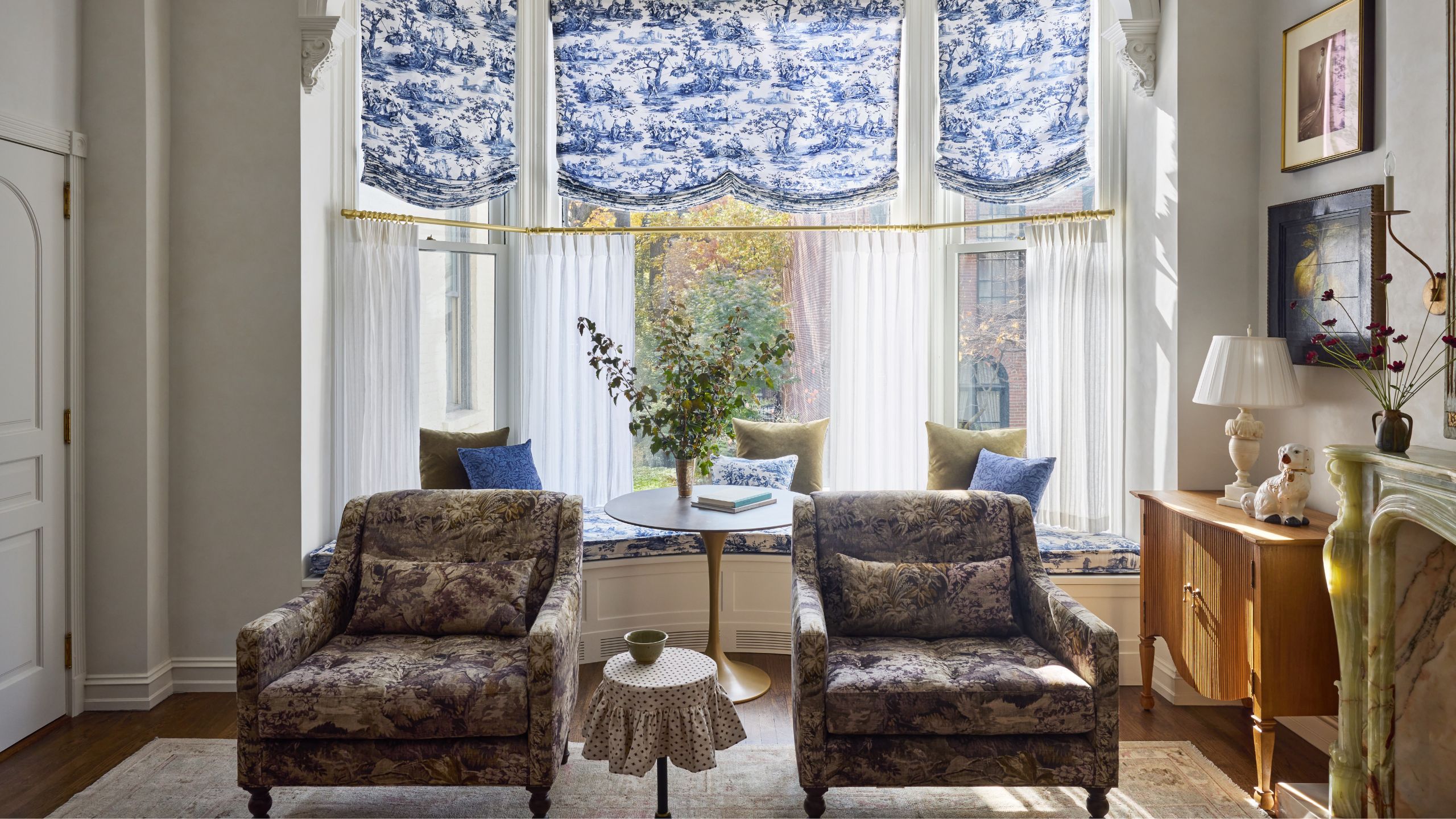 a grand 1900 Brooklyn apartment living room with a large bay window dressed with toile blinds and cafe curtains with vintage furnishings and marble fireplace