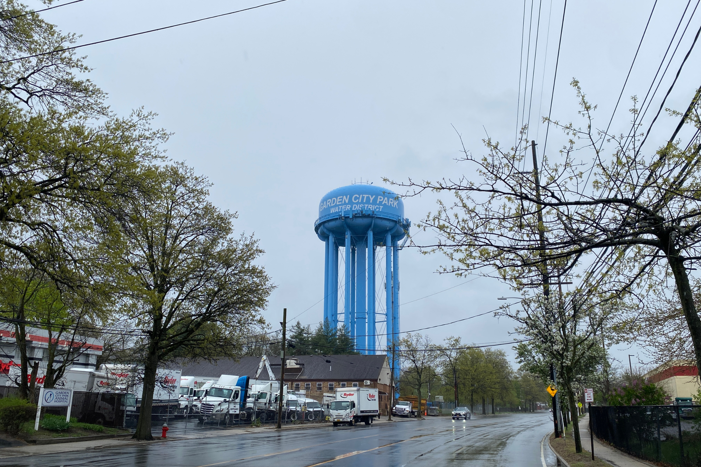 A water tower above a commercial street in Garden City Park on an overcast day.