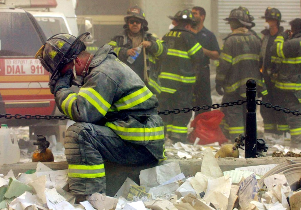 A firefighter in soiled gear sits with his head in his hands, surrounded by debris.