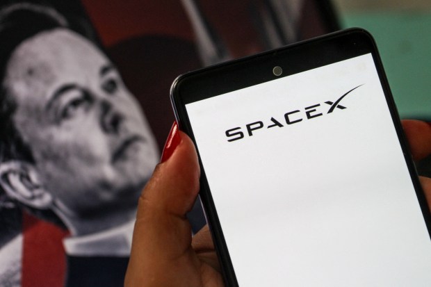 A smartphone displaying the SpaceX logo is shown in the foreground with a portrait of Elon Musk blurred in the arriere-plan in Tunis,Tunisia on July 11,2026. (Photo by Imen Ben Youssef / Hans Lucas / AFP via Getty Images)
