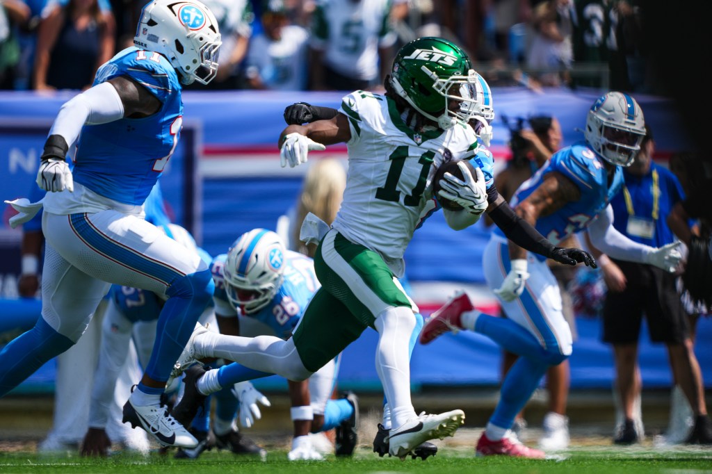 A New York Jets player in a green and white uniform with the number 11 runs with the football, surrounded by Tennessee Titans players in blue and white.