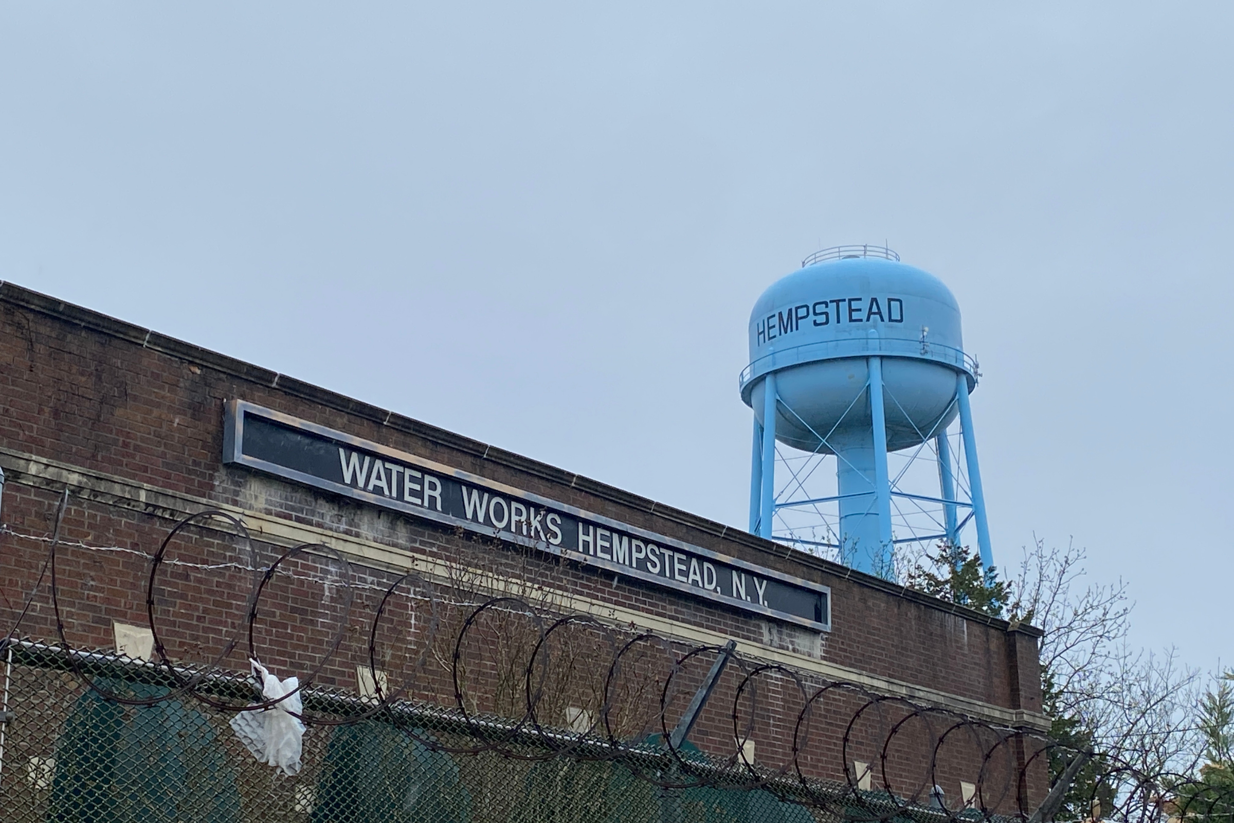 The Hempstead water works behind a fence, with the village water tower rising behind it.