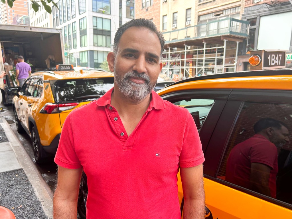 Bhupinder Dhillon stands smiling in front of his parked cab wearing a red polo shirt.