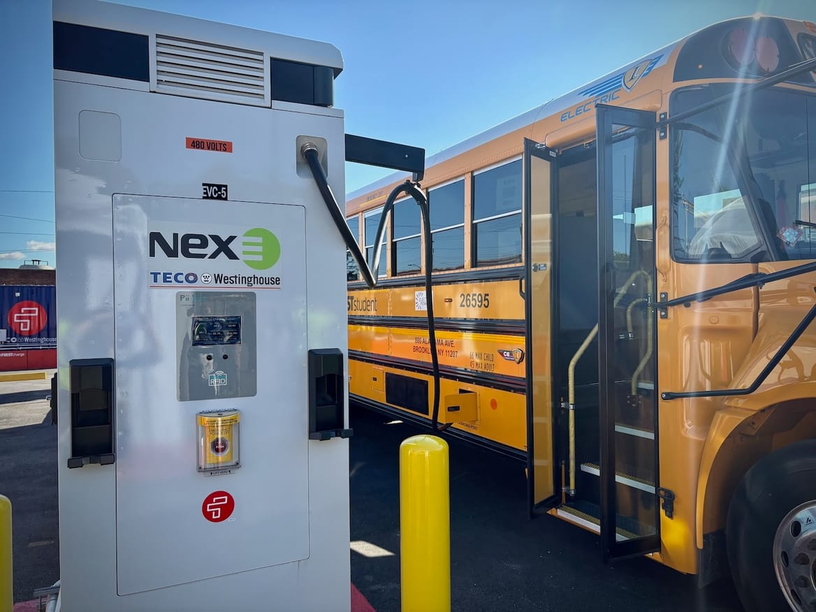 White battery with a school bus plugged into it; the bus door is open