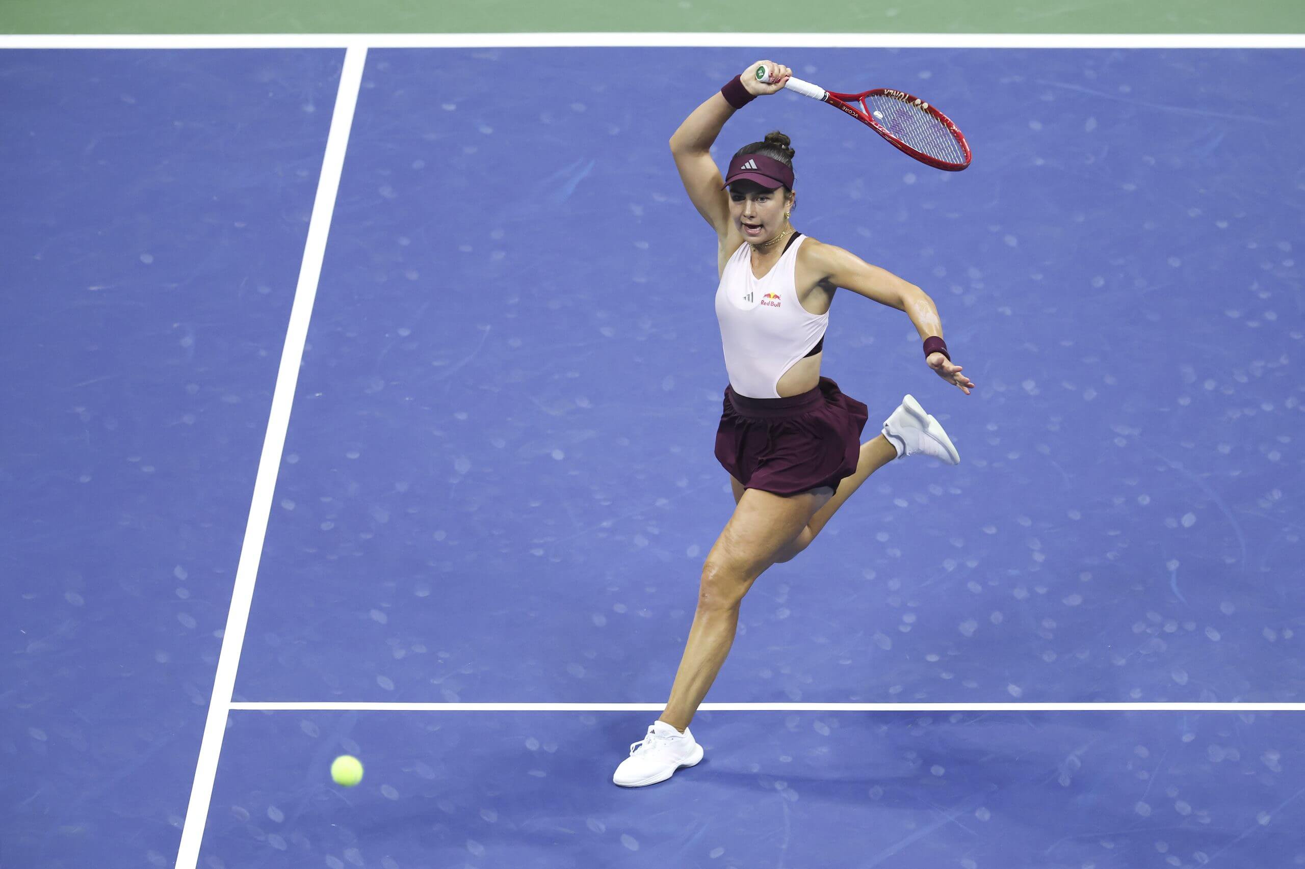 Iva Jović hits a forehand on the service line of a blue tennis court.