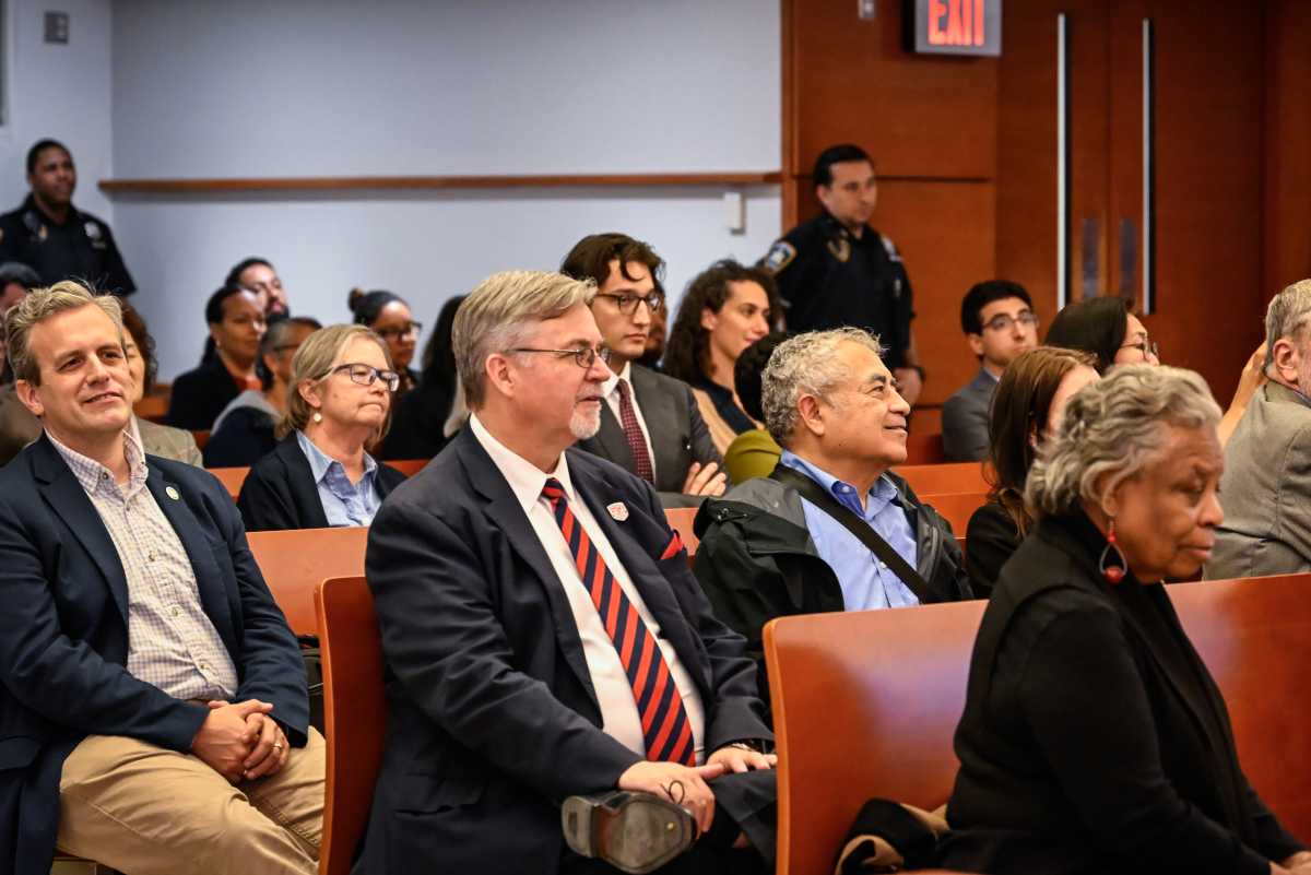A group of people are seated in a courtroom, attentively observing proceedings.