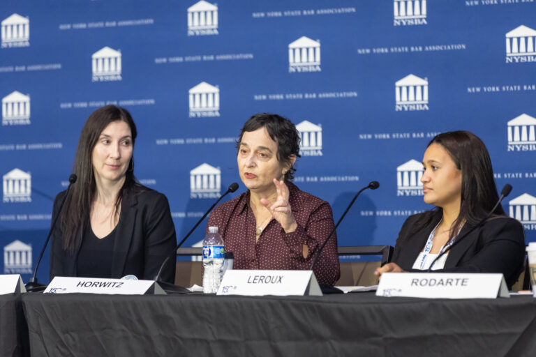 Three women sit at a panel table speaking into microphones, with a blue New York State Bar Association backdrop behind them. The woman in the center gestures while speaking. Name cards read Horwitz, Leroux, and Rodarte.