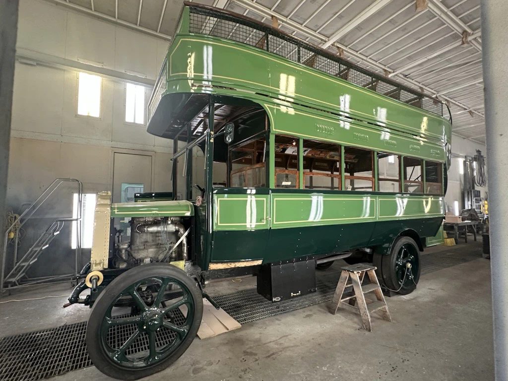 Restored vintage green double-decker bus inside a spacious garage, showcasing its classic design and exposed engine.
