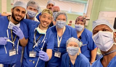 Nine doctors and nurses in scrubs, hair nets, masks and glove pose in a 'selfie' with one physician showing the pin that was removed from a patient's lung