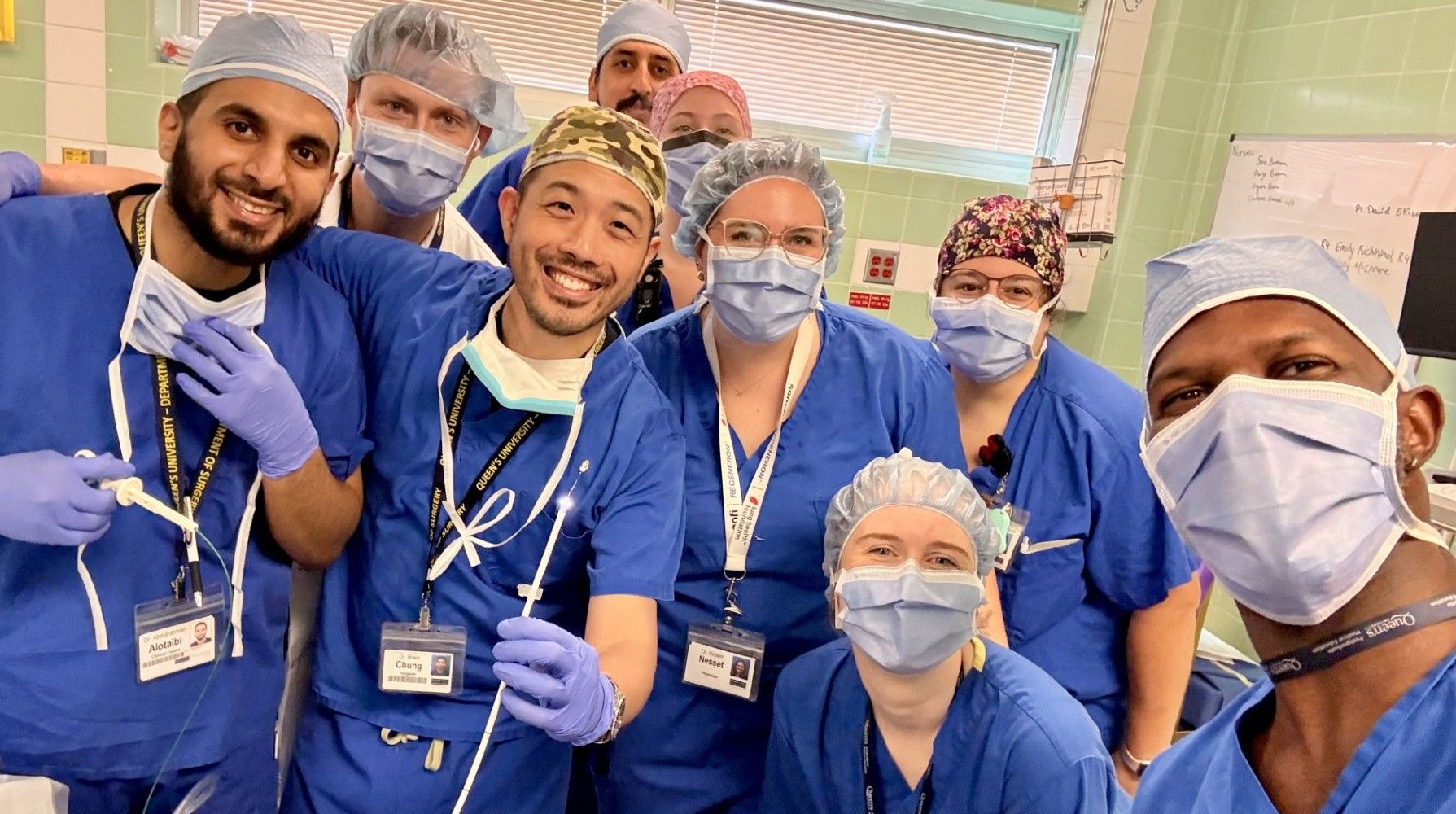 Nine doctors and nurses in scrubs, hair nets, masks and glove pose in a 'selfie' with one physician showing the pin that was removed from a patient's lung