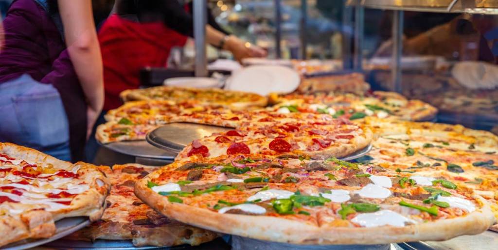 Pizzeria glass window. Variety of italian pizzas in a shop display, street food. Kitchen workers arranging the pizzas