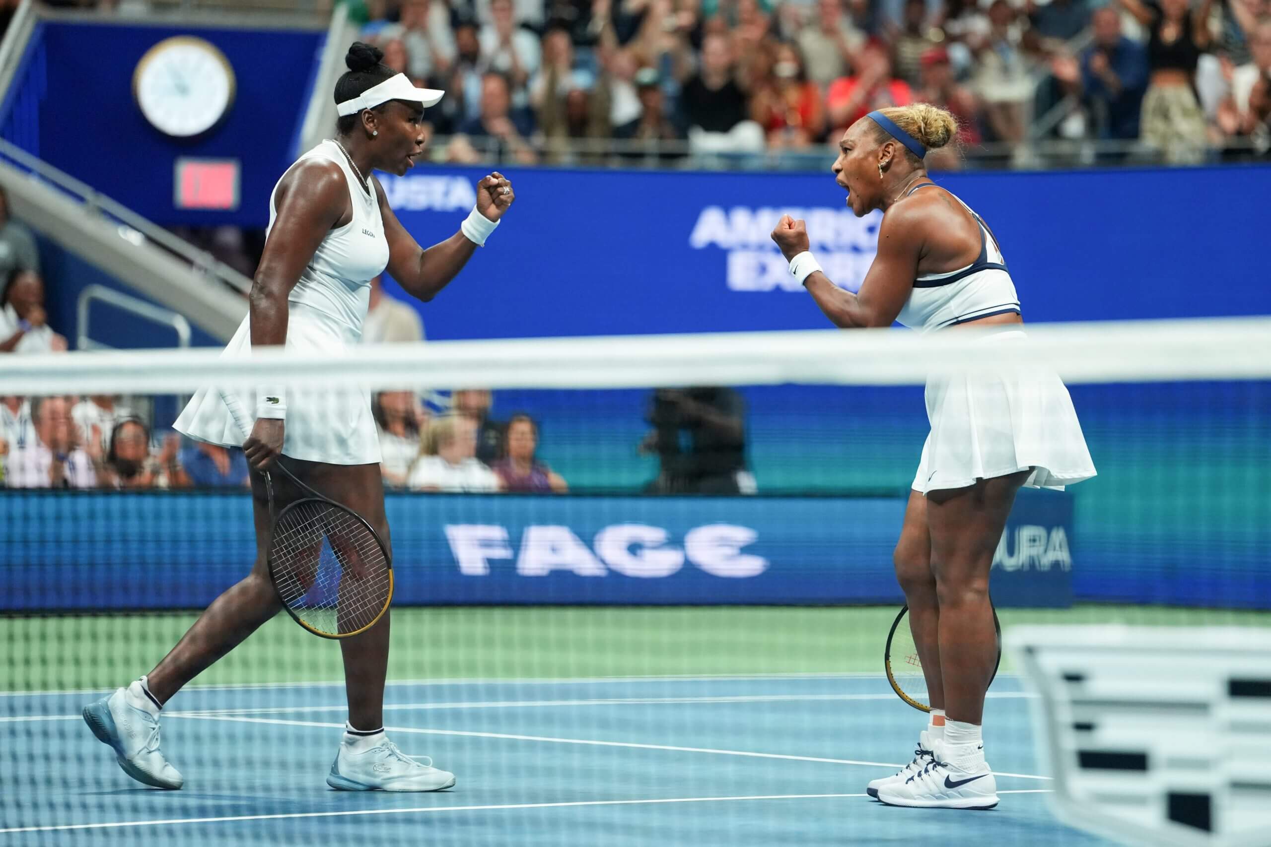 Serena and Venus Williams pump their fists as they walk toward each other on a tennis court.