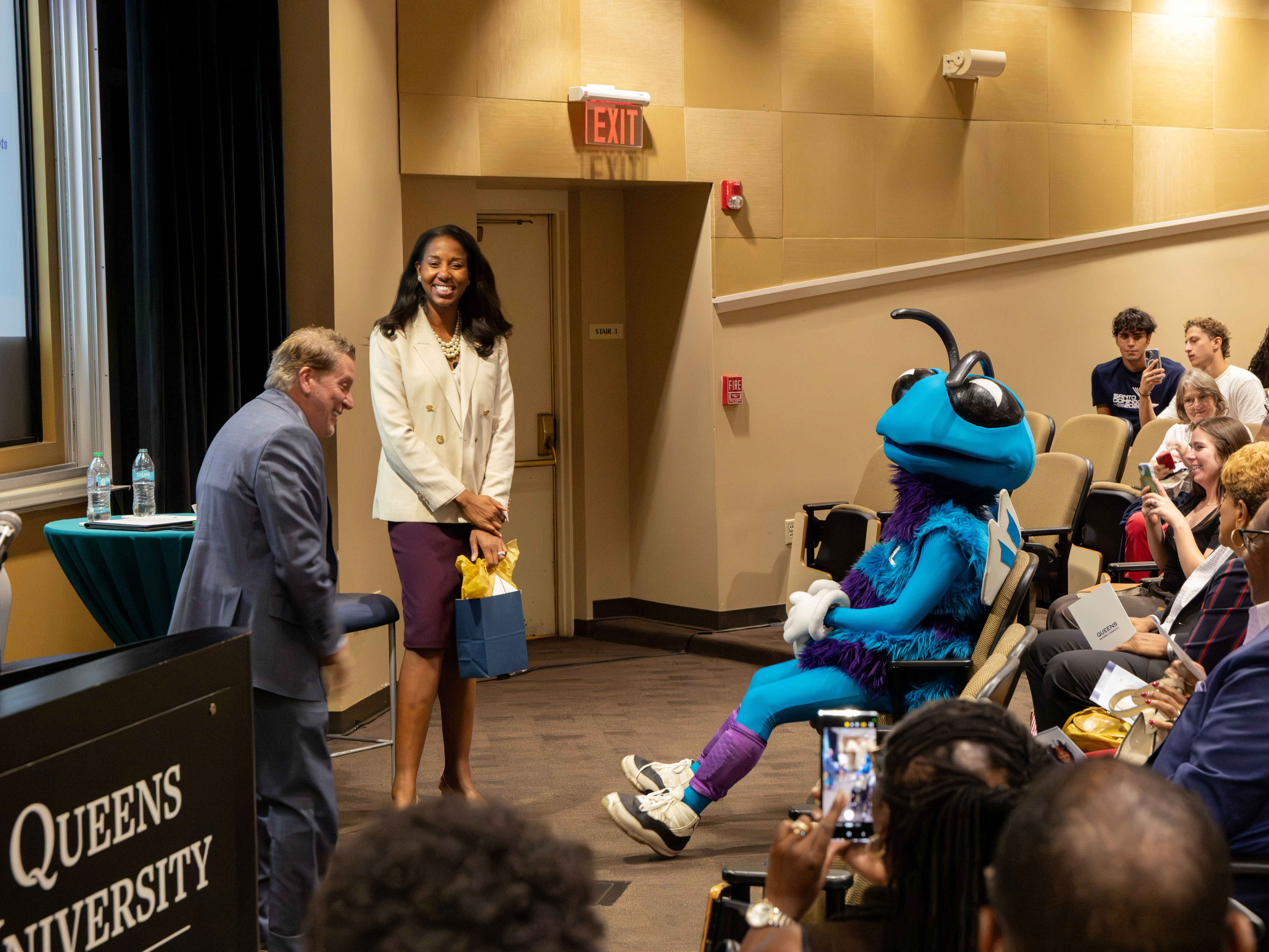 Teal and purple bee mascot sits front frow for a discussion between Will Sparks and Shelly Cayette-Weston.