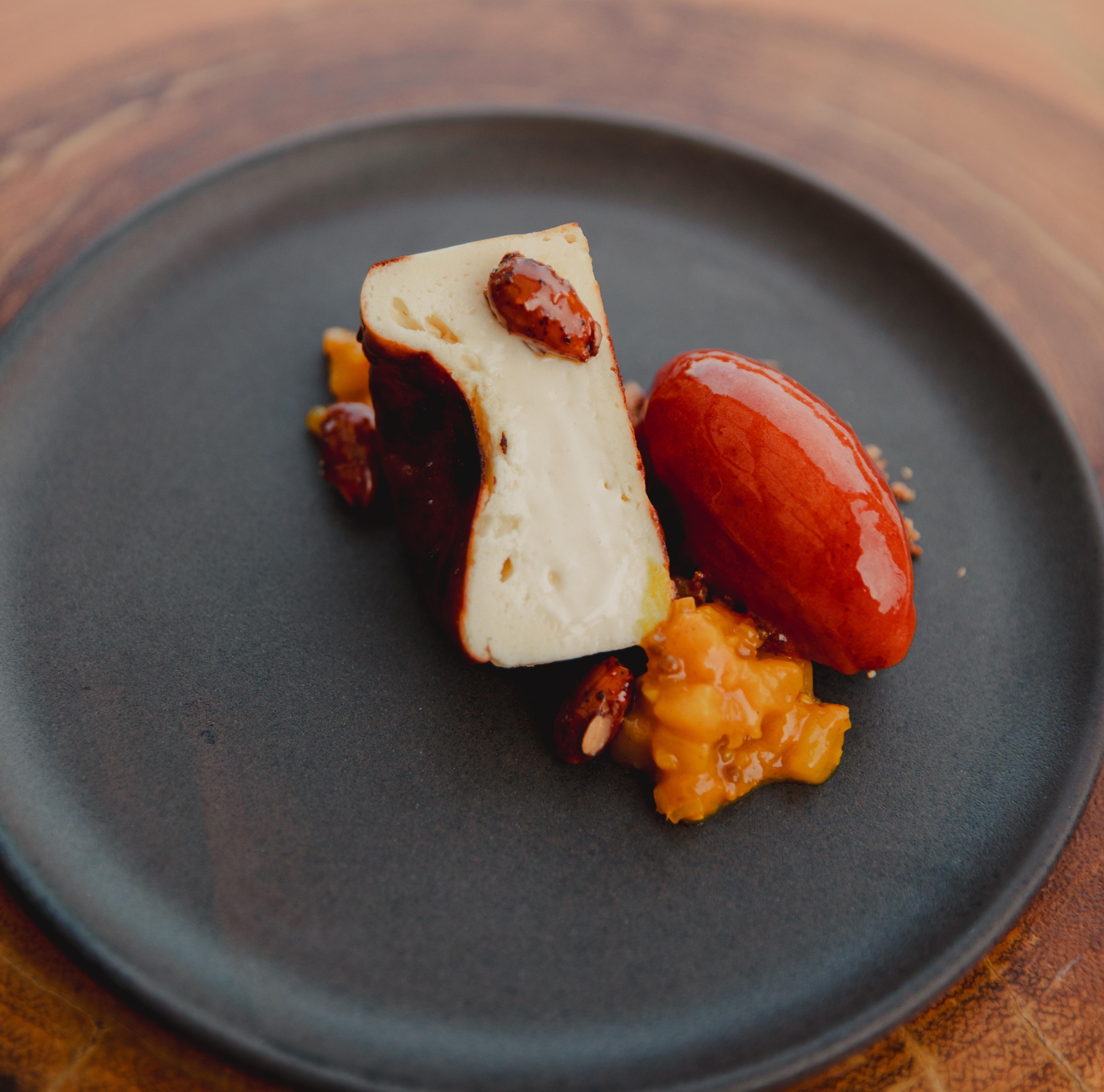 A slice of cheesecake on a plate with nuts and a scoop of red ice cream.