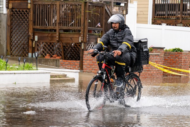 A delivery worker rides through flood waters in Howard Beach on Saturday, Sept. 26, 2026. (Theodore Parisienne / New York Daily News)
