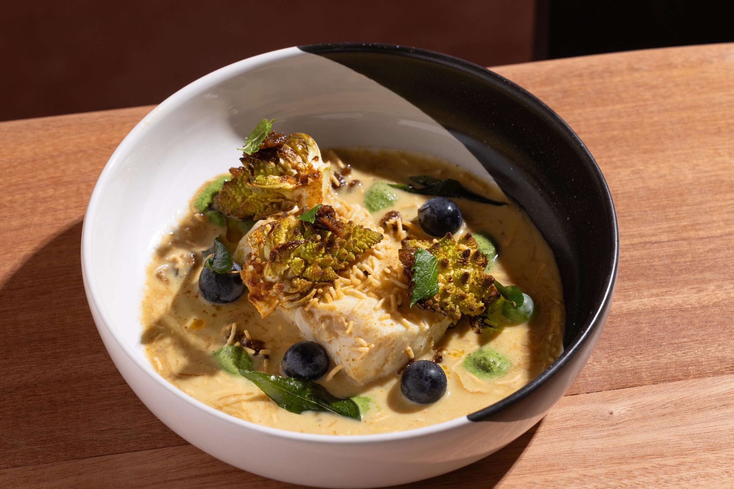 A bowl of yellow broth, green herbs, and fish chunks.