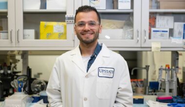 Topkaya stands in the lab at Upstate Medical University wearing a white lab coat.