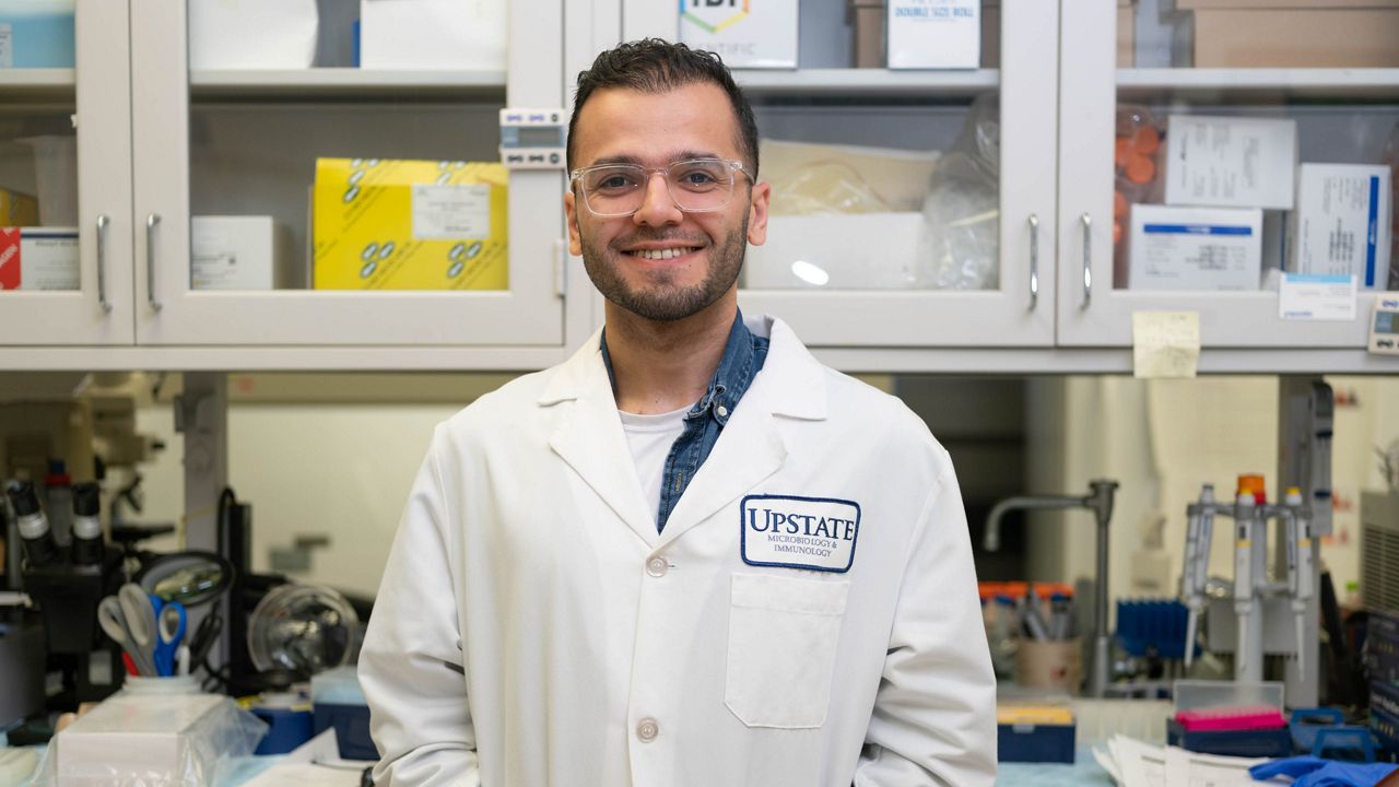 Topkaya stands in the lab at Upstate Medical University wearing a white lab coat.