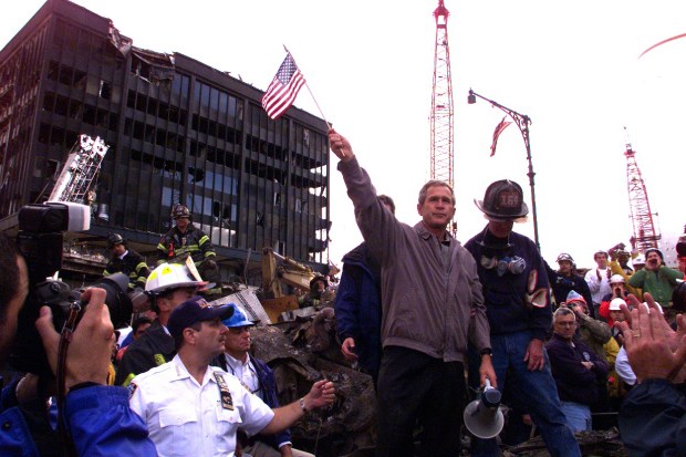 President George W. Bush, surrounded by rain-soaked rescue workers, waves an American flag from atop a wrecked fire truck in the midst of rubble of what was once the World Trade Center on Sept. 14, 2001. (Harry Hamburg / New York Daily News)