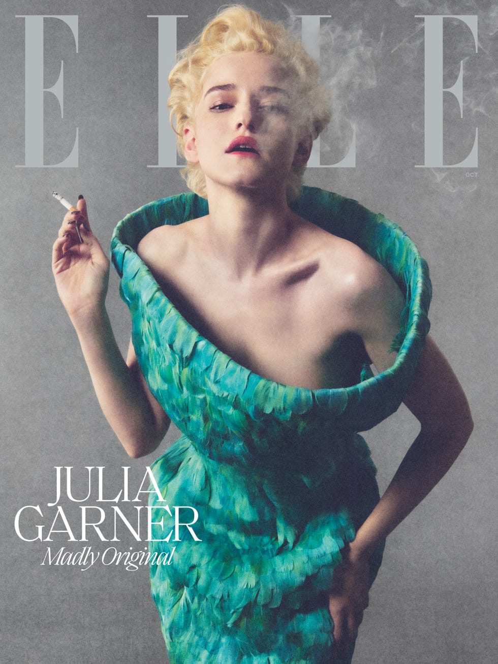 Julia Garner with blonde hair in a green feathered dress smoking a cigarette, featured on the cover of Elle magazine.